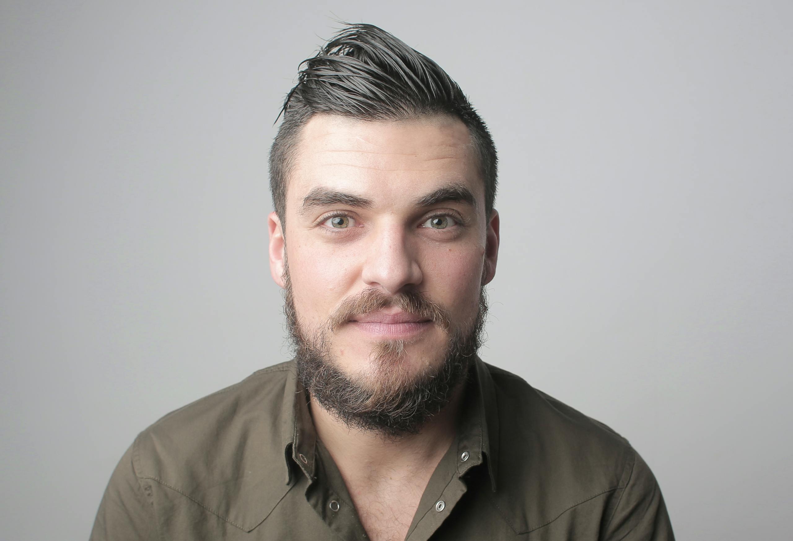 Close-up portrait of a man with a beard and styled hair, smiling warmly.